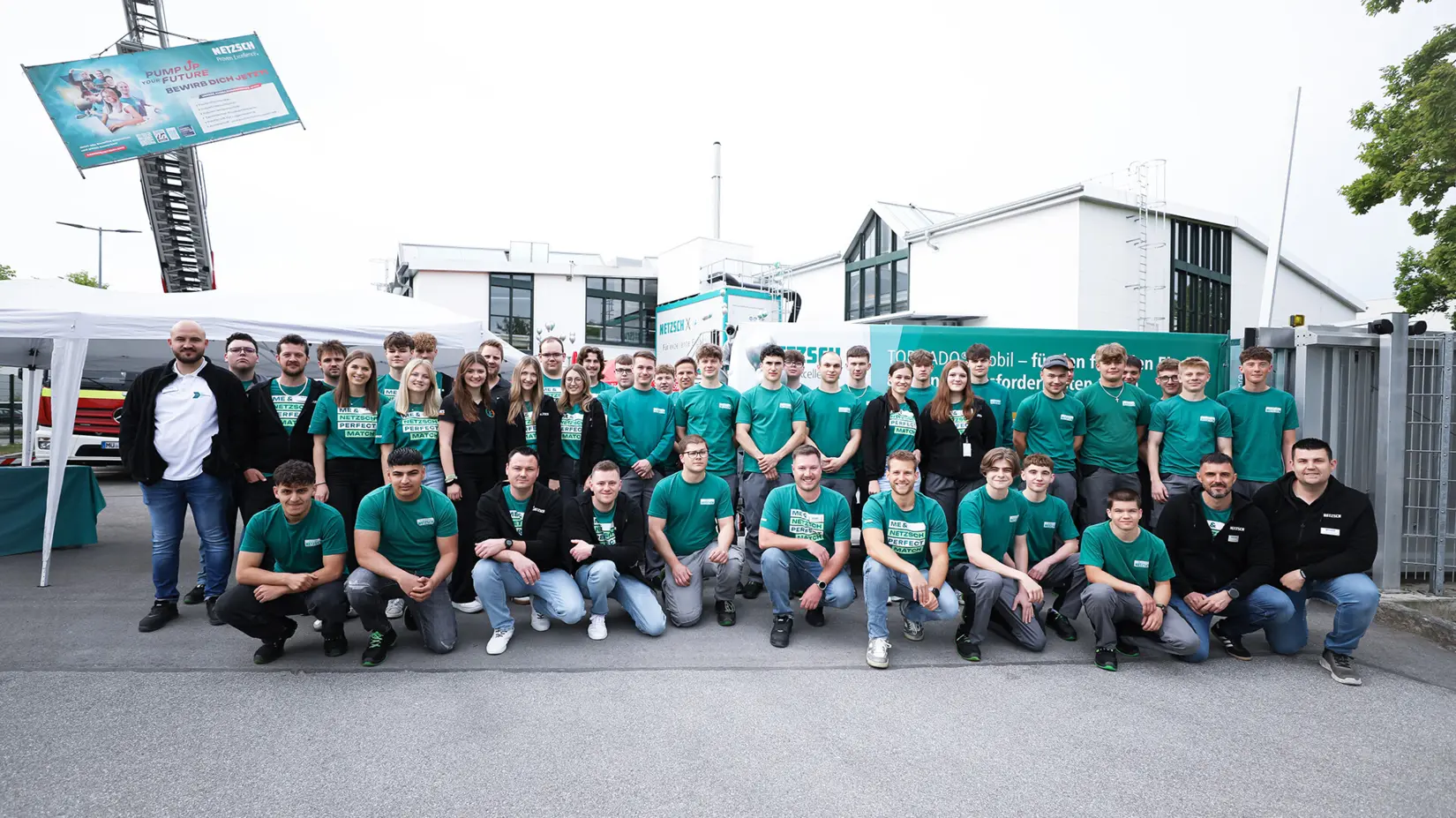 Group of apprentices and trainers wearing green NETZSCH shirts posing outdoors at the NETZSCH Pumps & Systems Day of Apprenticeship event.